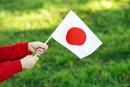 Hands of girl holding Japan flag. Independence Day concept. Green grass background.の写真素材