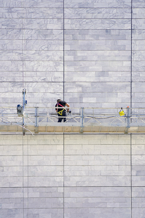 Installer in the construction cradle repair the facade of a house. Worker on a lift work on a construction of a multistory house. Construction worker on scaffoldの写真素材