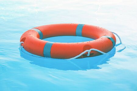 Orange lifebuoy pool ring float on blue water. Life ring floating on top of sunny blue water. Life ring in swimming poolの写真素材