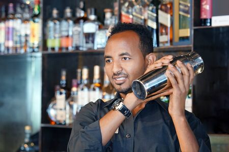 Professional african bartender male holding in hands a shaker with a fresh delicious cocktail....