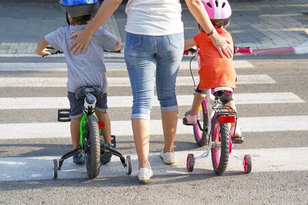 Mother goes pedestrian crossing with children on bicycles. A woman with children crossing the road in the city. Back view.の写真素材