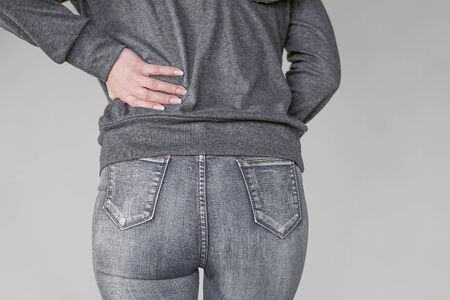 Close-up view of a young woman with pain in kidneys isolated on a gray background. Young woman with back ache clasping her hand to her lower back. Woman suffering from ribbing pain, waist pain.の写真素材