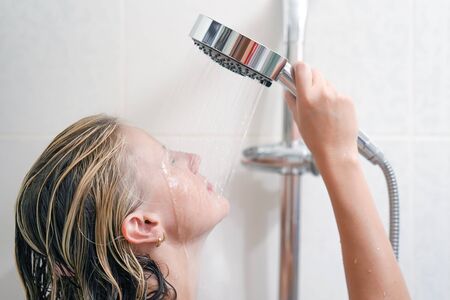 Relaxing woman in bathroom holds the shower in hands with stream of water. Portrait of a young woman in bathroom in shower. Nude woman in the bathroom.の写真素材