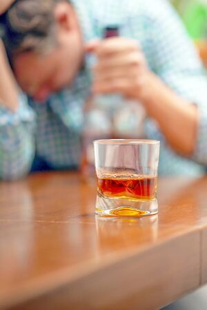 A glass of whiskey on the table on the background of a drunken man. Alcoholic fatherの写真素材