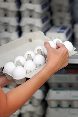 Hands woman with packages of white eggs in the store or supermarket. Woman buys eggs. Buying eggs at the grocery storeの写真素材