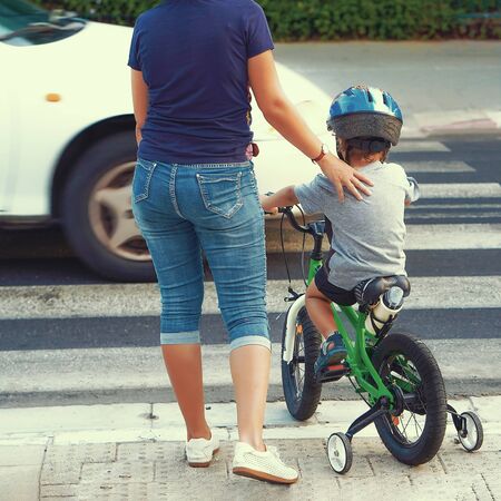 Mother goes pedestrian crossing with childr on bicycle. A woman with child crossing the road in the city. Back view.                                                                 の写真素材
