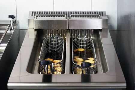 The cook fries french fries in a deep fryer. Preparation in a deep fryer. Deep fryer with boiling oil on restaurant kitchenの写真素材