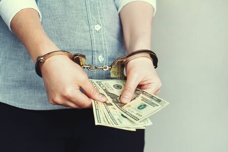 Office woman hand in handcuffs, holding a bribe. Arrested or arrested terrorist in handcuffs. Criminal hands locked in handcuffs. Closeup view. Hands in front. Selective focus. Toning.の写真素材