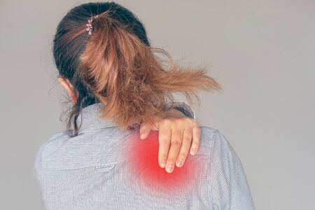 Woman suffering from neck pain isolated on gray background. A woman's sense of fatigue, exhausted, stressed.  Girl massages her painful neck with her hands. The concept of body and health. Tired neck.の写真素材
