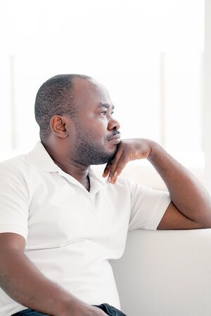 Portrait of a pensive african man. African American healthy male model. Handsome african man with a calm expression sitting on the sofa at home.の写真素材