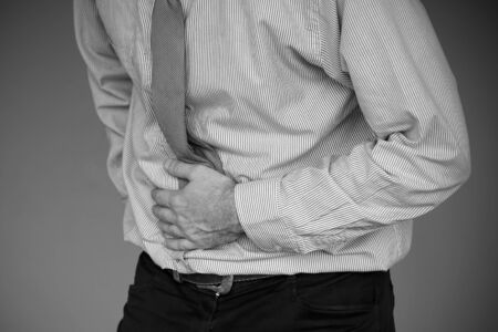 Black and white image of man holding his stomach in pain on gray background. Businessman suffering from abdominal pain. Body And Health Care Concept.                               の写真素材