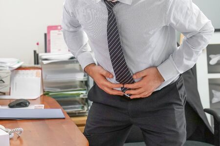 Close-up of office manager having painful stomachache. Chronic gastritis. Businessman with abdominal pain at his workplace in the office. Body And Health Care Concept.の写真素材