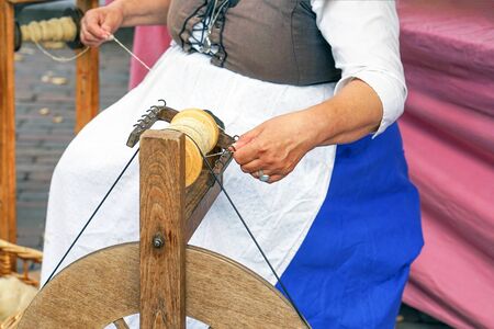 Craftswoman using an old spinning wheel to turn wool into yarn. Hands of a woman demonstrating traditional wool spinning on an old spinning wheel. Spinning on a spinning wheel. Spinning wheel.の写真素材