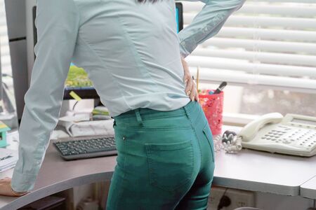 Woman in office suffer from low back pain isolated on gray background. Hand of woman holding her waist backache in pain. Woman suffering from ribbing pain, waist pain.                                 の写真素材