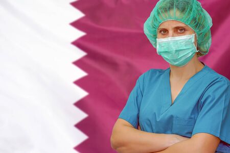 Female surgeon in mask and hat looks at the camera on the background of the Qatar flag. Health care and medical concept. Surgery concept and fight the virus in Qatar.の写真素材
