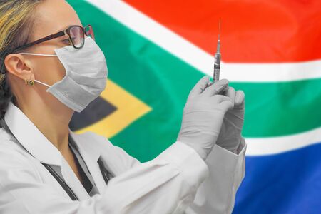 Female doctor or nurse in gloves holding syringe for vaccination against the background of the South Africa flag. Medicine concept and fight the virus. Coronavirus in South Africa.の写真素材