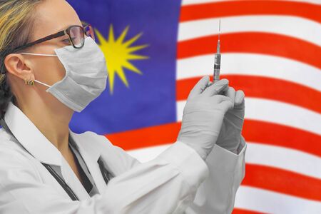 Female doctor or nurse in gloves holding syringe for vaccination against the background of the Malaysia flag. Medicine concept and fight the virus. Coronavirus in Malaysia.の写真素材