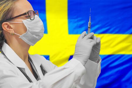 Female doctor or nurse in gloves holding syringe for vaccination against the background of the Sweden flag. Medicine concept and fight the virus. Coronavirus in Sweden.の写真素材