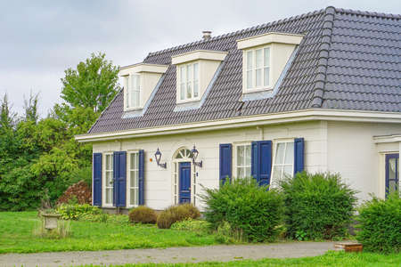 Old classical white house on blue cloudy sky background. Private house for families with children. Two story white home with porch. Beautiful private house with a lawn of green grass. Netherlands.のeditorial素材