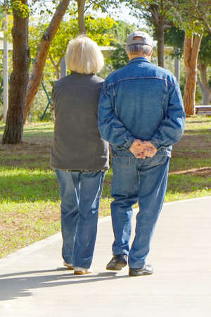 A pair of elderly people walking in the park. Elderly women and man walk in park. Back view