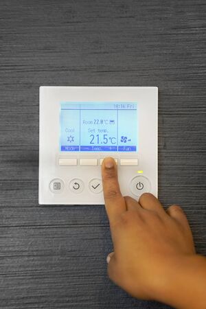 African female hands on the air conditioning control panel. Hand girl setting temperature air condition. African woman hand try to turn on the new air condition in room, in the hotel room.の写真素材