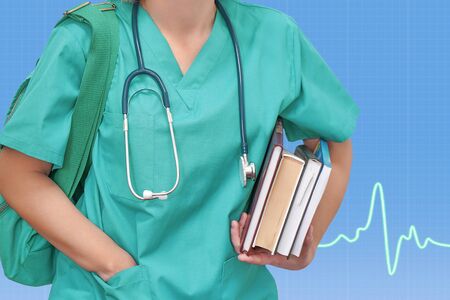 Fmale nurse or intern surgeon in blue uniform with books and bag on blue background electrocardiogram. Health care banner. Education concept.の写真素材
