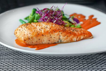 Closeup perfectly executed Norwegian salmon fillet steak with crispy fish skin, broccoli, young beans and spicy red sauce on table in restaurant. Plate with a dish of Norwegian salmon fish.の写真素材