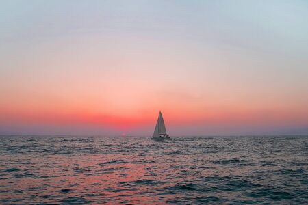 Sailing boat in the sea during red sunset. Yachting as a luxury sport and great vacation.の写真素材