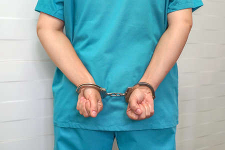 Crime in medicine, surgeon or doctor in blue uniform with handcuffed hands at the back. Criminal...