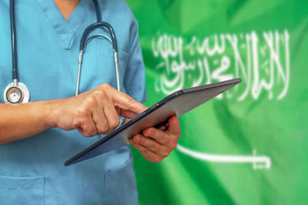 Surgeon or doctor using a digital tablet on the background of the Saudi Arabia flag. Medical equipment or medical network, technology and diagnostics in Saudi Arabia.の写真素材