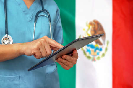 Surgeon or doctor using a digital tablet on the background of the Mexico flag. Medical equipment or medical network, technology and diagnostics in Mexico.の写真素材