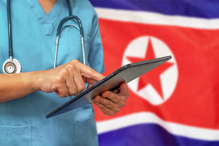 Surgeon or doctor using a digital tablet on the background of the North Korea flag. Medical equipment or medical network, technology and diagnostics in North Korea.の写真素材