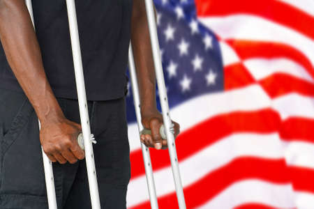 African man on crutches on the background of the USA flag. Disabled veterans of the US Army. The concept of stop violence and racism in USAの写真素材