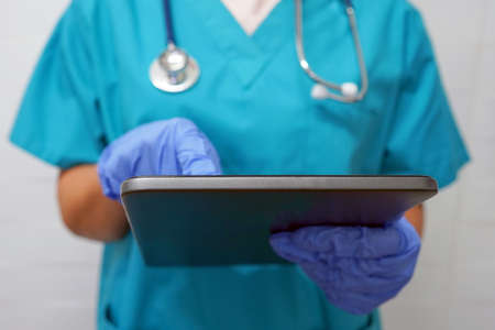 Surgeon or doctor woman in gloves using digital tablet. Surgeon in gloves writes texting on digital...