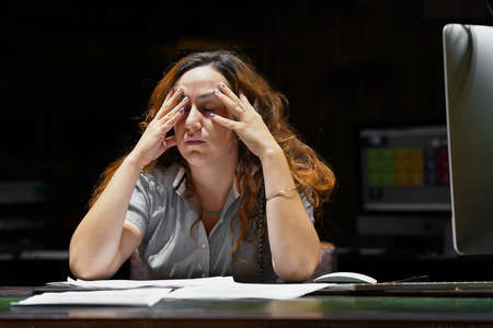 Woman office worker is distressed with a lot of paperwork. A lot of paper work in office. Night time