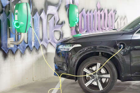 Electric car charging on parking lot with electric car charging station. Close up of power supply plugged into an electric car being charged. 31 August 2018. Parking area. Amsterdam. Netherlandsのeditorial素材