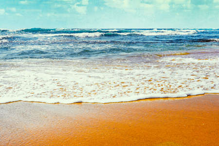 Sea surf to the beach shore sunny day summer. Sea water runs onto the sandy shore. Blue waves on a sandy beach. Sandy beach with ocean tidal waves breaking on a sand beach splashingの写真素材