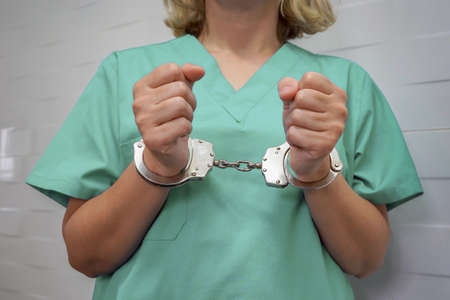 Surgeon in green uniform with handcuffed hands. Criminal medic woman hands locked in handcuffs.