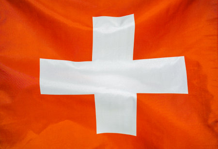 Fabric texture flag of Switzerland. Flag of Switzerland waving in the wind. Switzerland flag is depicted on a sports cloth fabric with many folds. Sport team bannerの写真素材