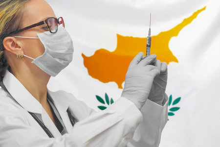 Female doctor or nurse in gloves holding syringe for vaccination against the background of the Cyprus flag. Medicine concept and fight the virus. Coronavirus in Cyprus.の写真素材