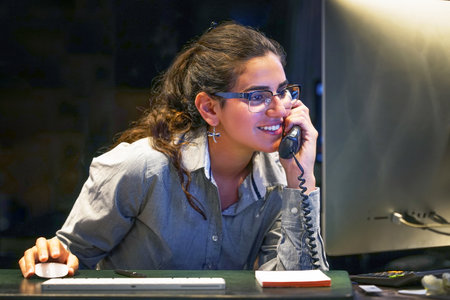 Portrait of office worker, manager woman secretary answering phone calls and talking with customers. Night time. The concept of serviceの写真素材