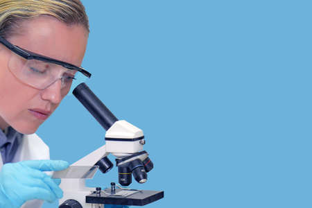 Female biochemist student looking through microscope in the lab at the university. Medical...