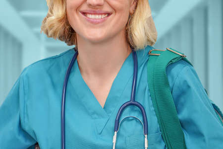 Fmale nurse or intern surgeon in blue uniform with books and bag on the background of a blurred corridor of the clinic. Health care banner. Education conceptの写真素材
