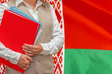 Woman holding red folder on Belarus flag background. Education and jurisprudence concept in Belarusの写真素材