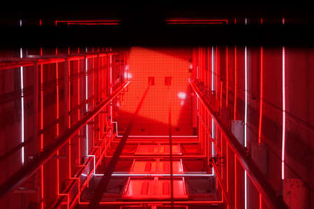 Lift shaft in a residential building. Elevator corridor in the building lit by red elumination. Futuristic elevator shaft is located in a high tower. Abstract, background. Bottom view.の写真素材