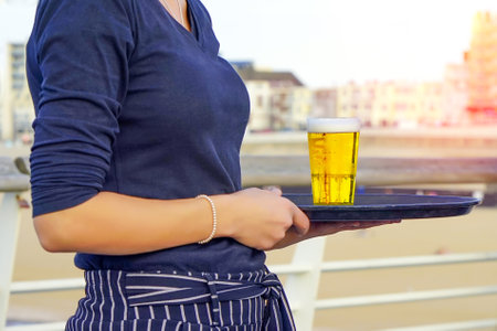 Waitress carries a glass of beer on a tray at a beach restaurant. September 2, 2018. Den Haag. Netherlandsの写真素材