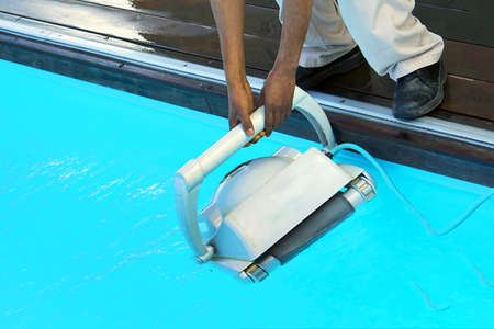 A pool cleaner holds a robot cleaner. Pool cleaner during his work. African hotel staff worker cleaning the poolの写真素材