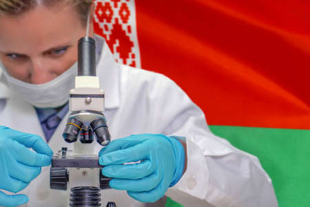 Female biochemist looking through a microscope against Belarus flag background. Medical technology and pharmaceutical research and development of science concept in Belarusの写真素材