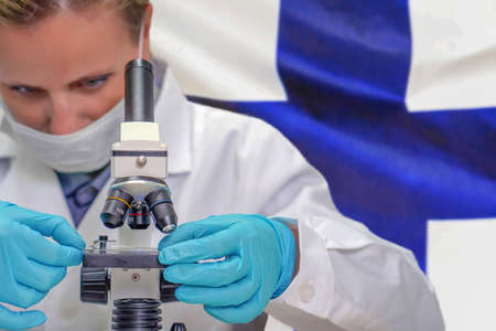 Female biochemist looking through a microscope against Finland flag background. Medical technology and pharmaceutical research and development of science concept in Finlandの写真素材