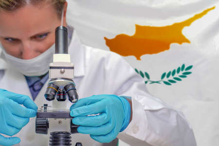 Female biochemist looking through a microscope against Cyprus flag background. Medical technology and pharmaceutical research and development of science concept in Cyprusの写真素材